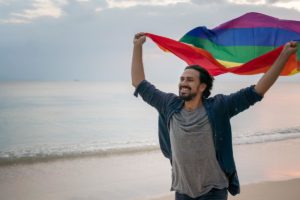 man on beach waving rainbow flag after rehab
