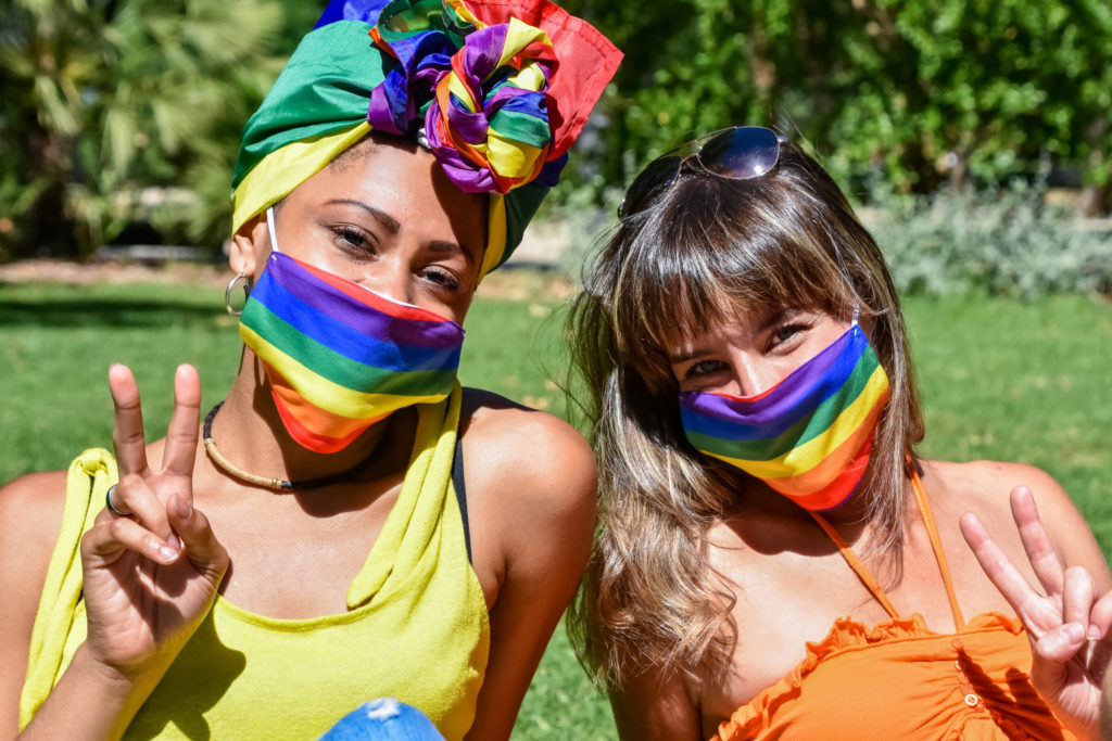 LGBTQ New Year's Resolution. Two attractive women of different races wearing rainbow face masks make peace signs with their hands. LGBTQ Pride day celebration in pandemic times.