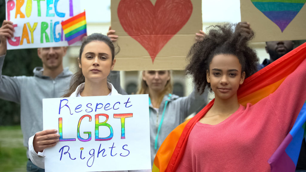 LGBTQ New Year's Resolution. Group of people raising rainbow flags, posters for LGBTQ rights, gender equality)