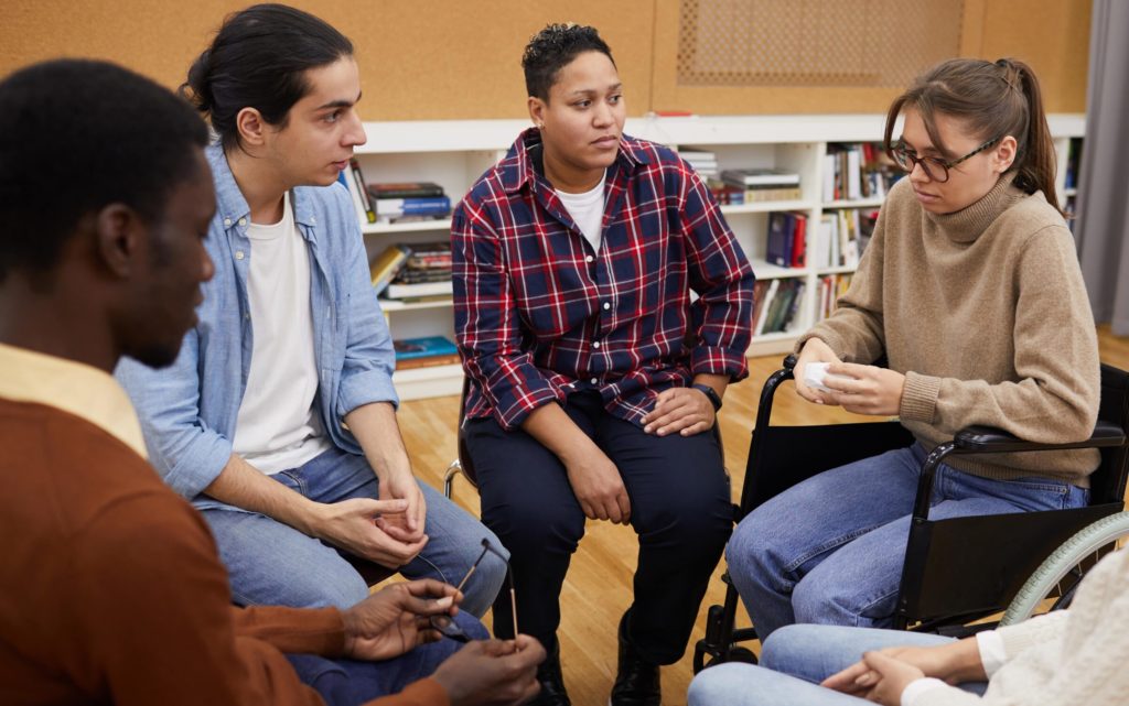 A couple of people sits in a circle and comforts a woman by placing hands on her back.