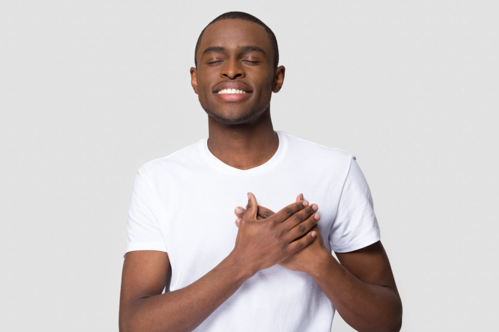 A man wearing a white shirt covering his heart with his hands.