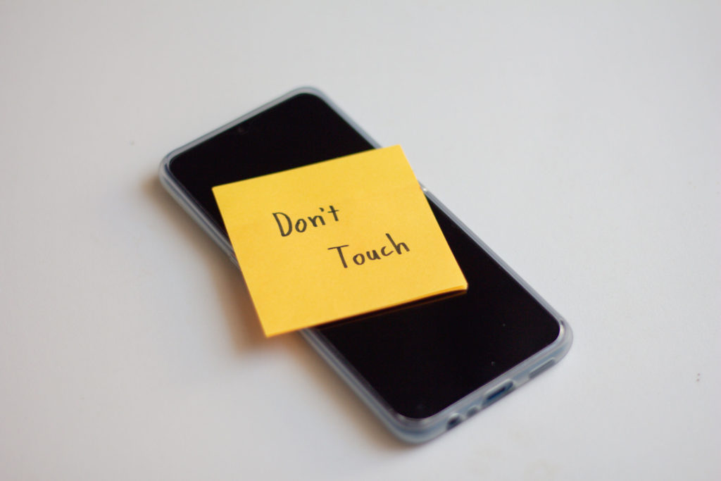 A cell phone with an orange sticky note saying 'Don't Touch.'