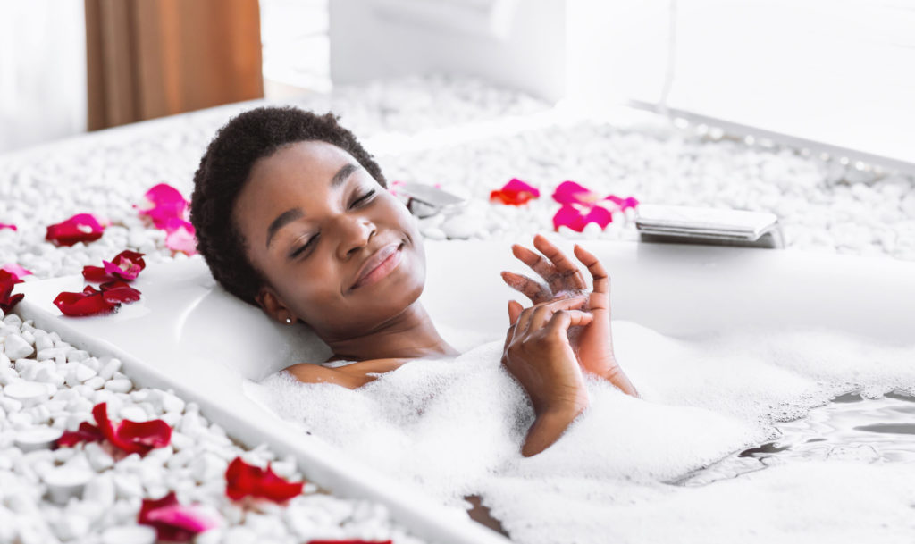 A woman laying in a bubble bath surrounded by rose petals.