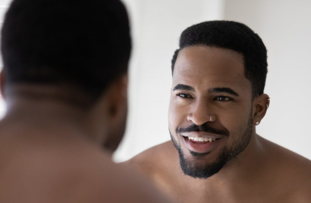 A young African American man looking in the mirror smiling. 