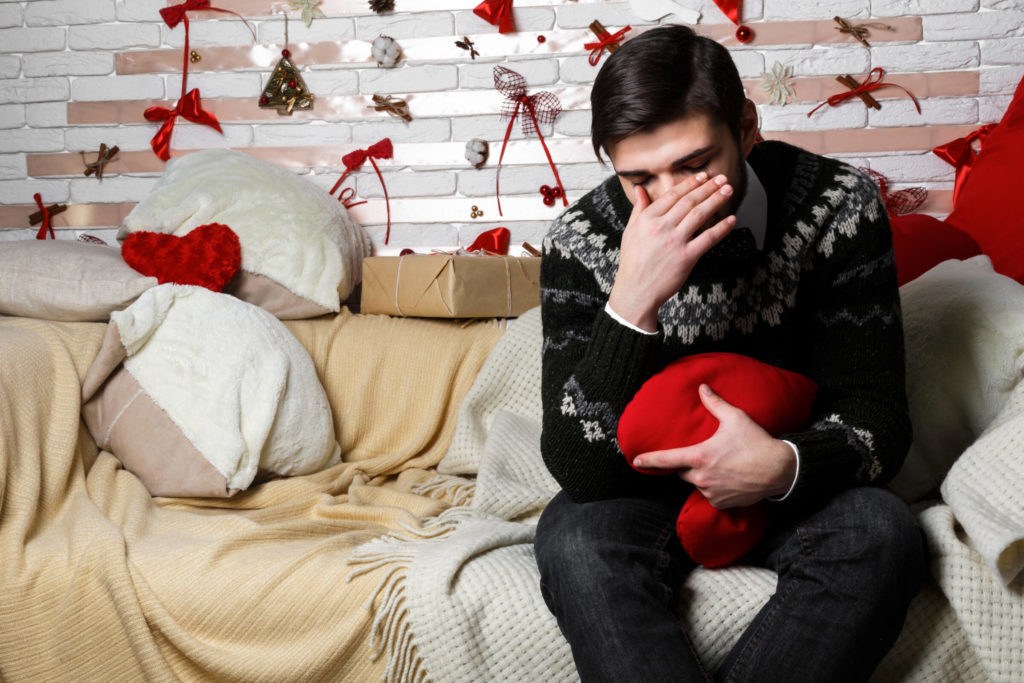 A man surrounded by red decorations sitting on a couch with his hand covering his eyes.