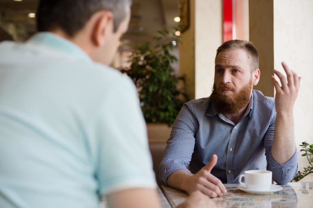 two people sit at a table and talk possibly in a rehab alumni program