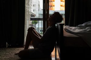 a person sits on the floor leaning against a couch possibly needing meth addiction treatment