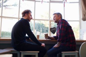 two people sit at a table talking possibly in an alumni program