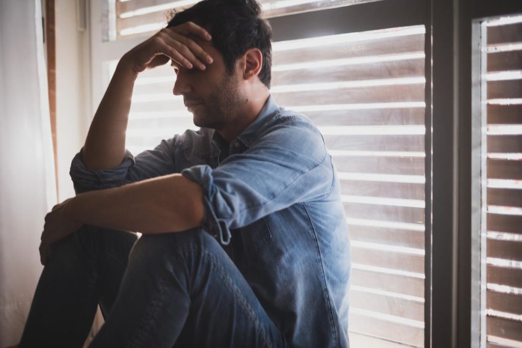 troubled man sitting in dimly lit room wondering what does meth do to someone with adhd