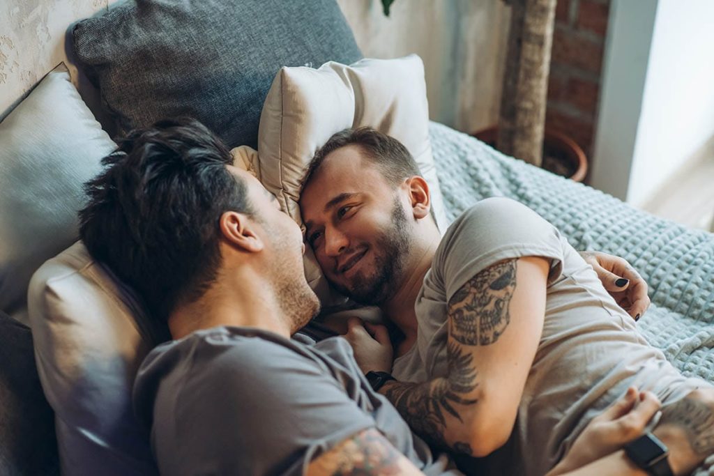 two men laying in bed together and facing one another as they discuss 12 tips to help come down from a high