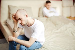 young man sitting on edge of bed facing away from his partner who is in bed and has learned how to recognize meth smell