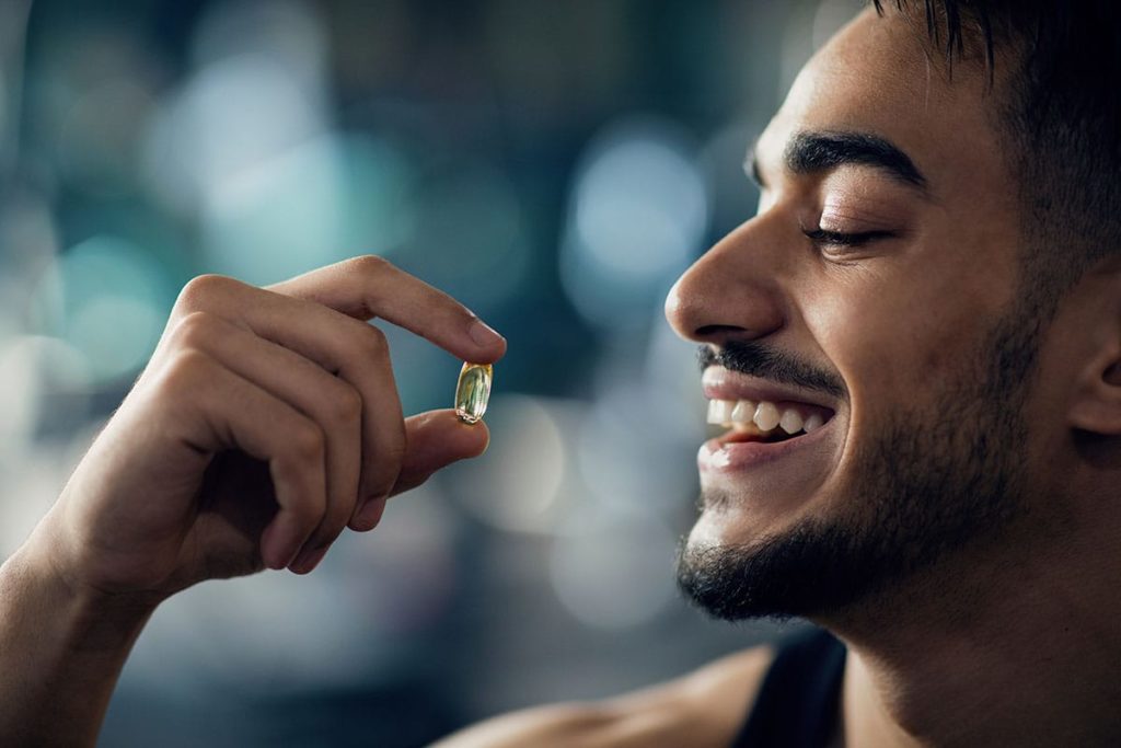 smiling young man about to take a vitamin as part of the key vitamins and supplements for meth recovery