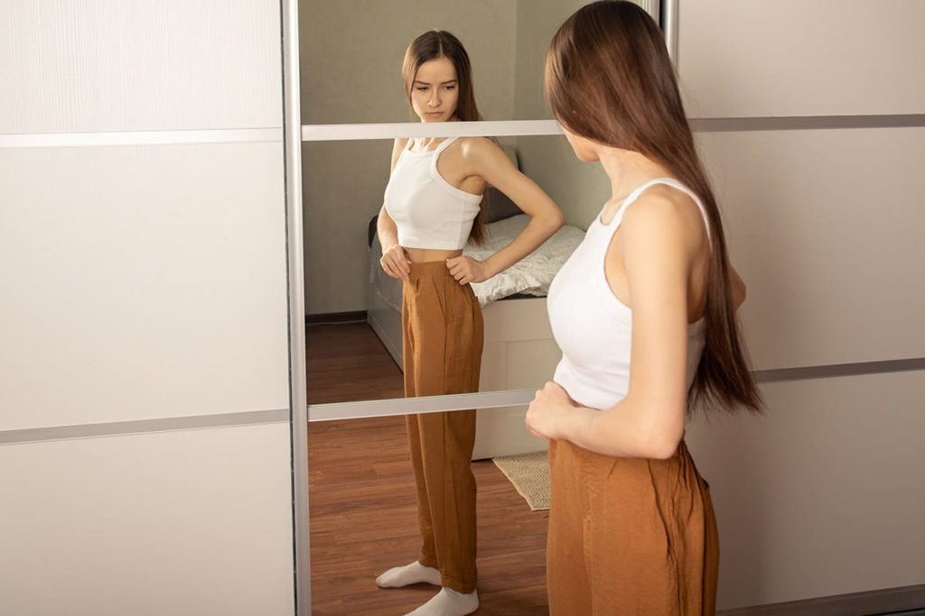 young woman studying her body in the mirror unaware of the dangerous relationship between meth and weight loss