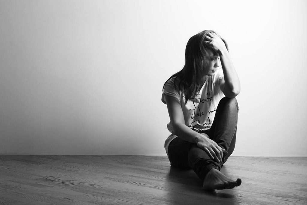 black and white image of teenage girl sitting in bare room displaying signs and symptoms of heroin use