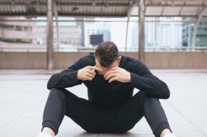 man sitting on ground outside with head in his hands wondering what is dual diagnosis and how is it treated