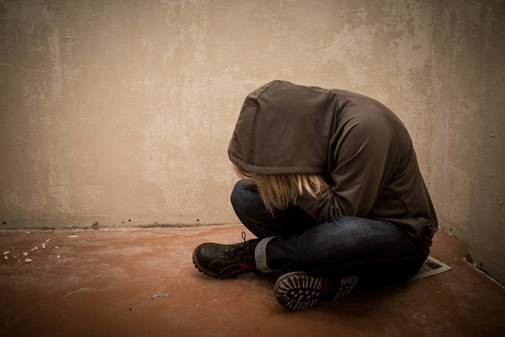 image of person in a jacket with hood drawn and sitting on the floor curled into a ball demonstrating how substance abuse impacts mental health