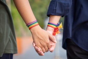 Two hands holding, both wearing LGBTQ bracelets