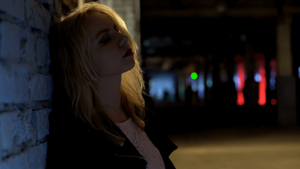 young woman leaning against alley wall at night after partying and contemplating party drug addiction rehab