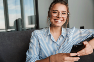 young woman smiling and playing on her phone after benefitting from sober living programs.