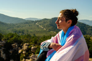 Person covered with trans flag sitting on mountain